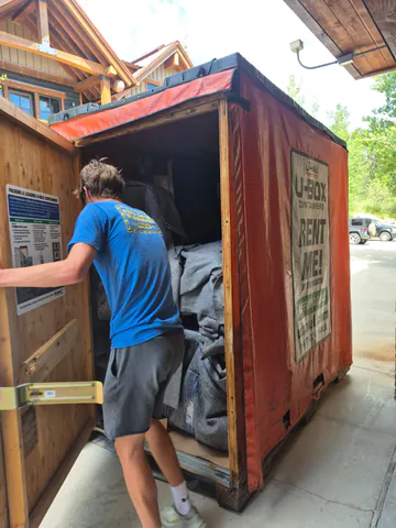 Mover in a blue Smoove Mooves shirt loading protected furniture into a moving container